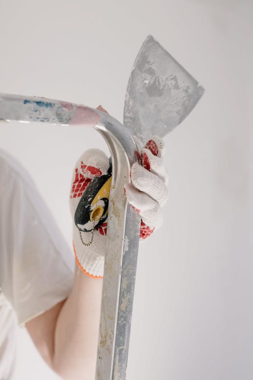An image of a gloved hand, holding a drywall mud spatula tool